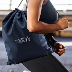 Person holding a navy drawstring bag with 'Copper Fit' logo in an indoor setting.